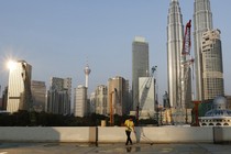 A worker sweeping the ground in front of skyscrapers