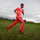 A Black man, dressed in all red workout clothing, running across a grassy field