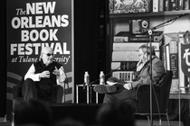 A black and white photo of an two older men with beards talking on a stage.