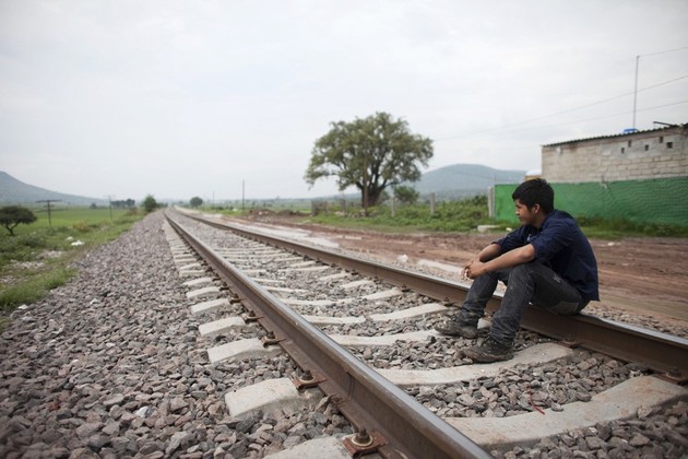 A man sits on train tracks and looks off into the distance.