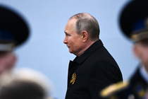 Putin, frowning, strides past men in military uniform.