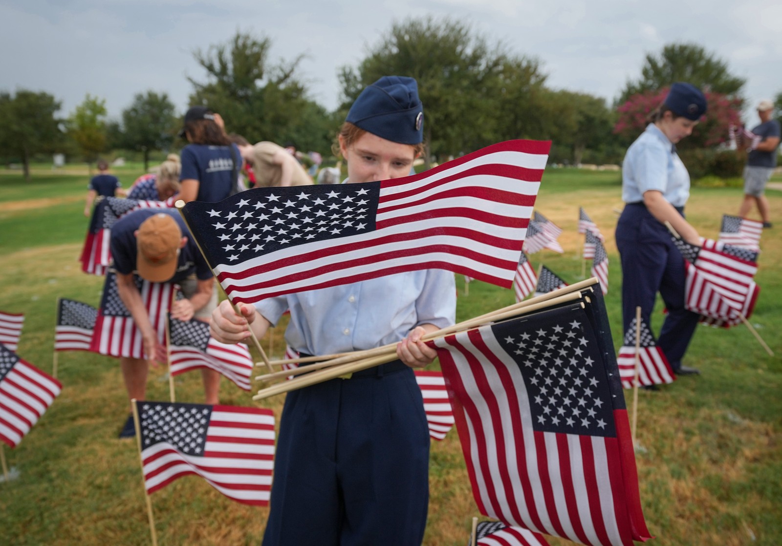 Young people, some in uniform, place American flags in a park.