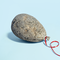 A photo realistic illustration of a balloon shaped rock with a red ribbon attached.