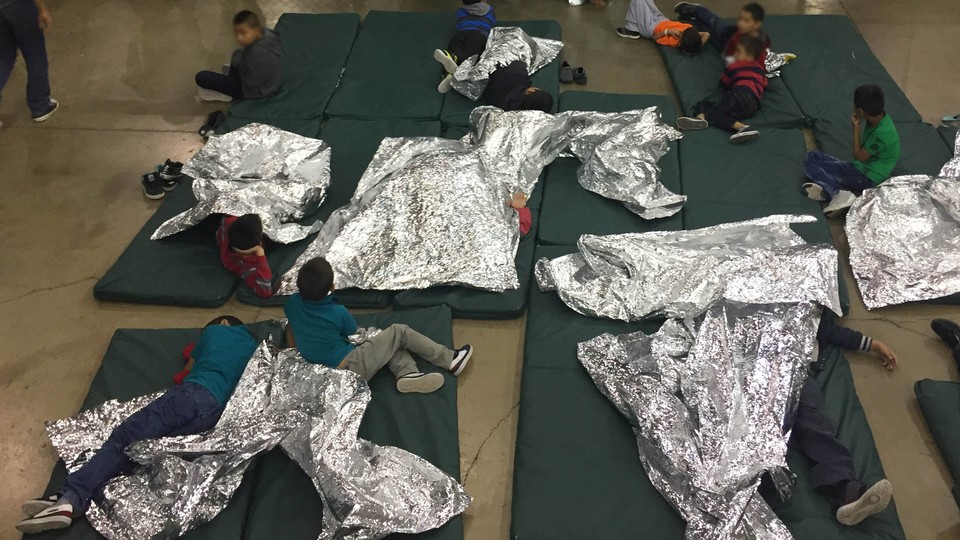 Children lie on green mattresses on the floor and use silver space blankets.