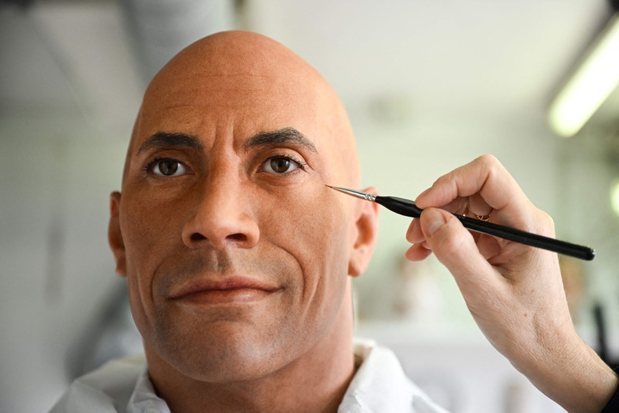 A person uses a fine paintbrush on the face of a wax figure of actor Dwayne Johnson.