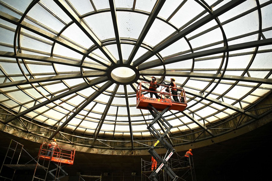 Several construction workers are seen beneath a large circular opening in a ceiling.