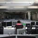 A worker sits alone in a dimly lit office, surrounded by computer monitors