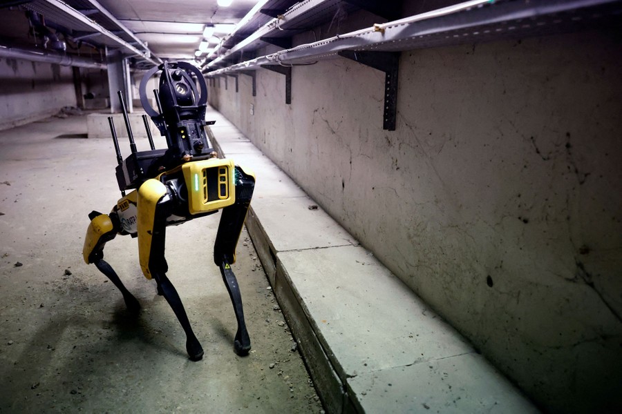 A four-legged robot carries equipment in a concrete-walled room.