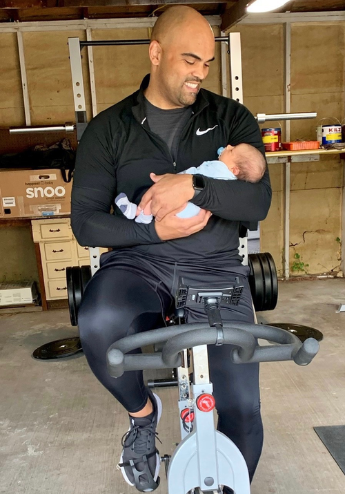 A photo of Colin Allred on an exercise bicycle holding a baby
