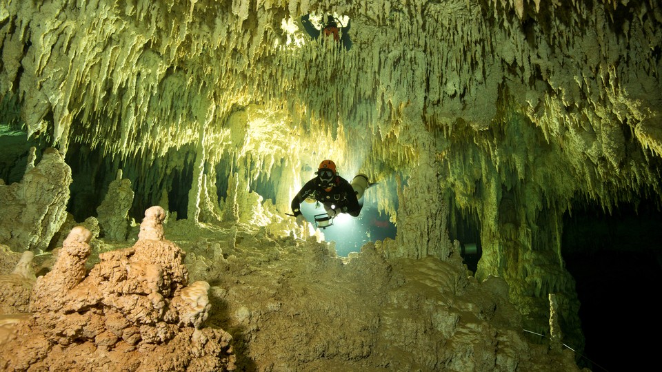 A scuba diver measures the length of an underwater green and brown cave system