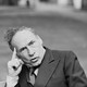 Mel Brooks, his head leaning and his index finger touching his temple, while he offers a funny expression.