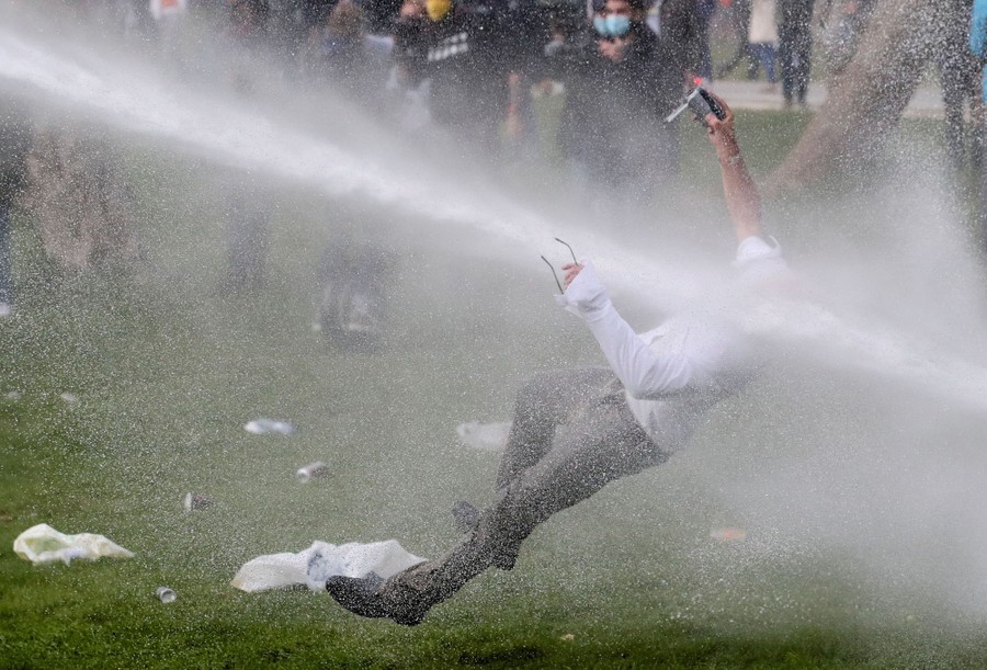 A person is knocked to the ground, struck by the strong jet of a water cannon.