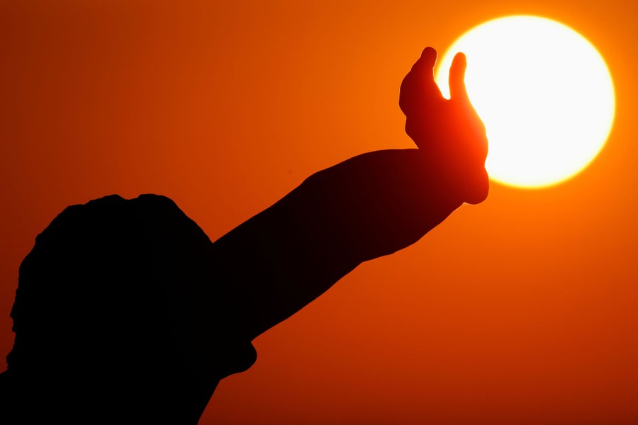 A statue's hand is seen with the sun in the background.