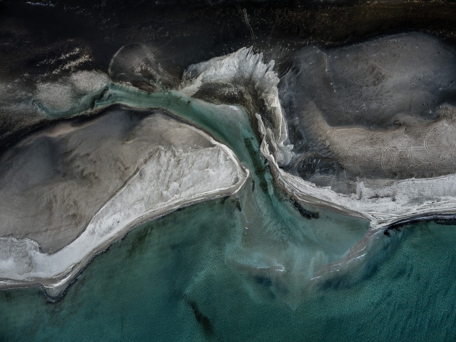 aerial photograph of otherworldly shoreline with shades of black, gray, and blues