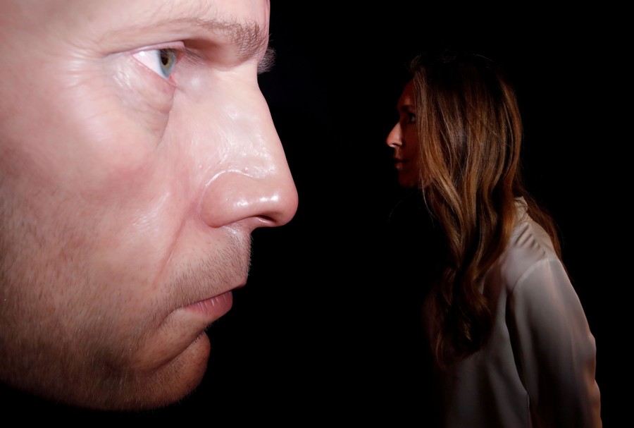 A person looks closely at a larger-than-life-size sculpture of a face.