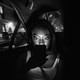 A passenger looks at their phone in the backseat of a dark car.