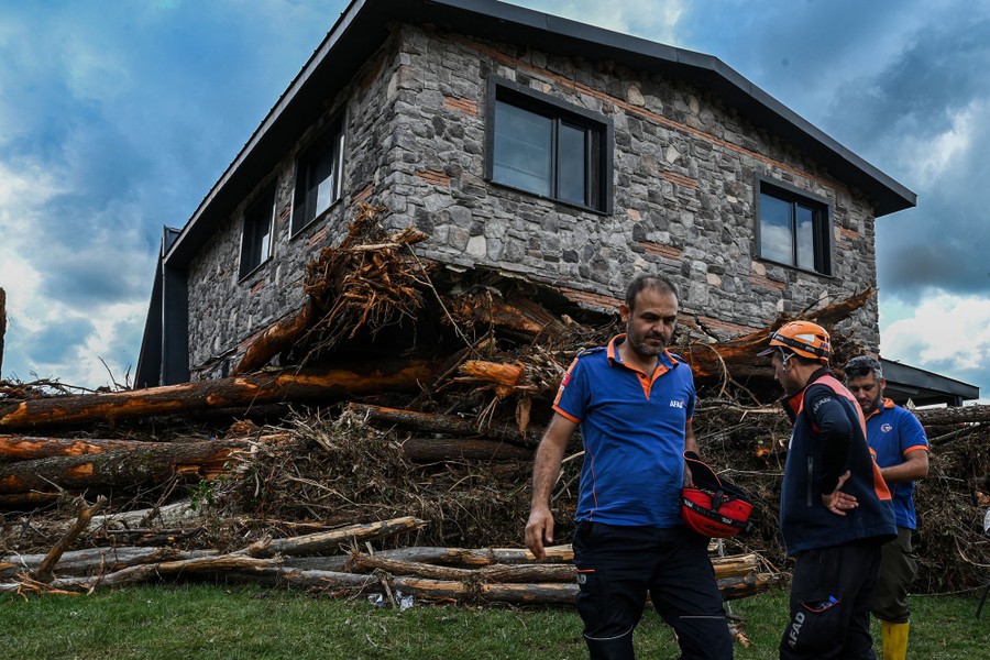 Several rescue workers stand beside a pile of toppled trees pushed up under a house.