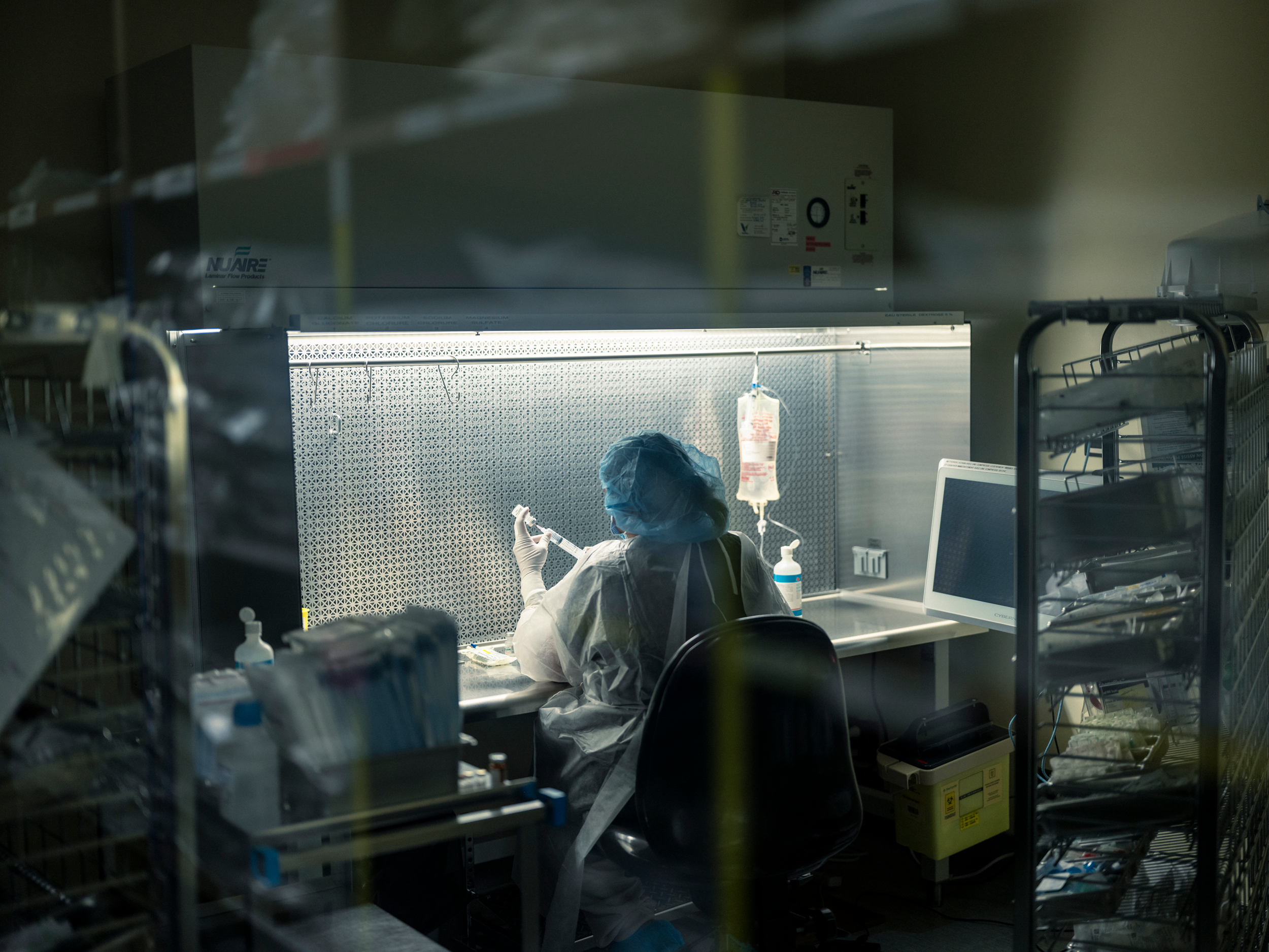 photo of person wearing protective medical gear and sitting at brightly lit desk in darkened room holding syringe