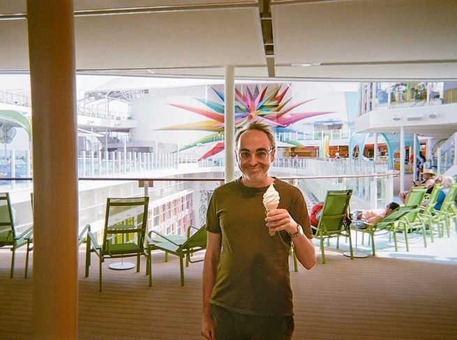 photo of author smiling and holding soft-serve ice-cream cone with outdoor seating area in background