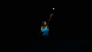 A photo of Serena Williams with a black backdrop tossing a ball