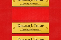 A red wall with three gold nameplates for President Donald J. Trump