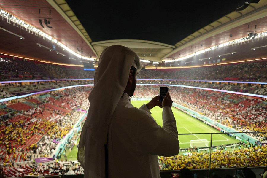 A person uses their phone to take a photo of a partly-full sports stadium.