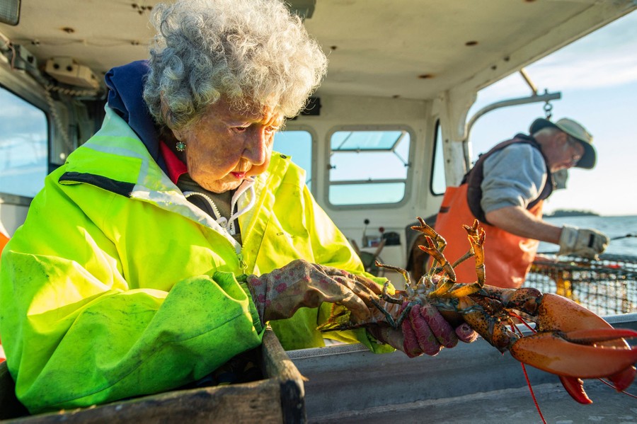A woman handles a lobster aboard a small boat.