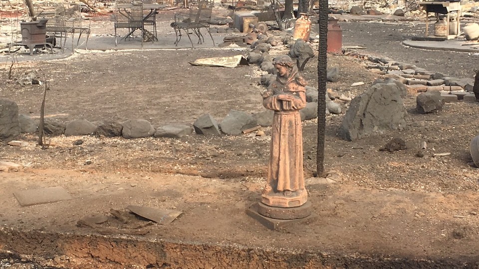 A statue stands in a backyard, amidst the rumble of a destroyed home. 