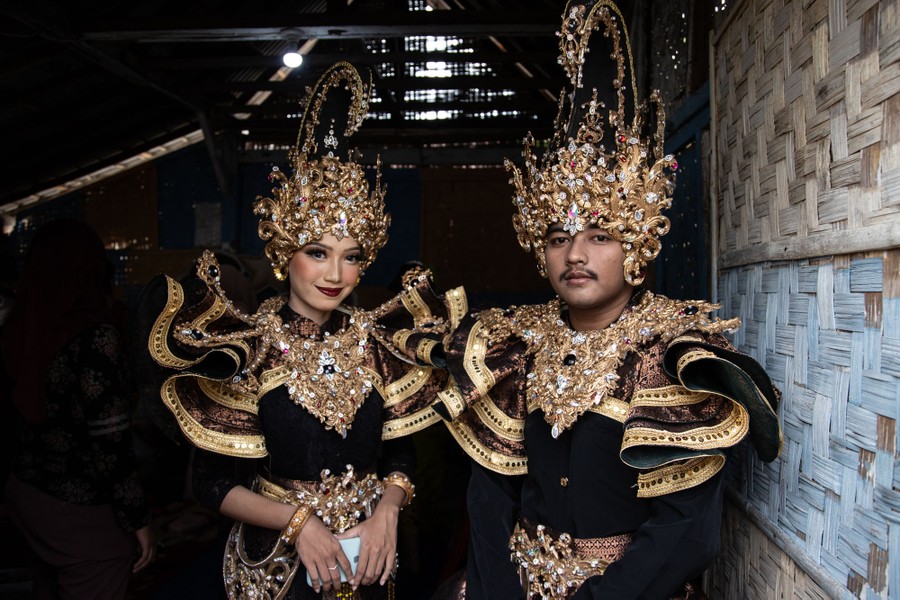 Two performers pose, wearing ornate jeweled costumes and headgear.