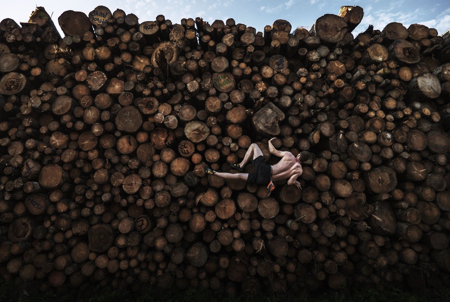 A rock climber scales the side of a large pile of logs.