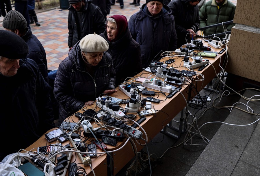 Several people sit in front of a table covered in cords, chargers, and mobile devices.