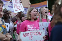 A view of several people in a larger crowd, marching and carrying pro-abortion-rights signs.