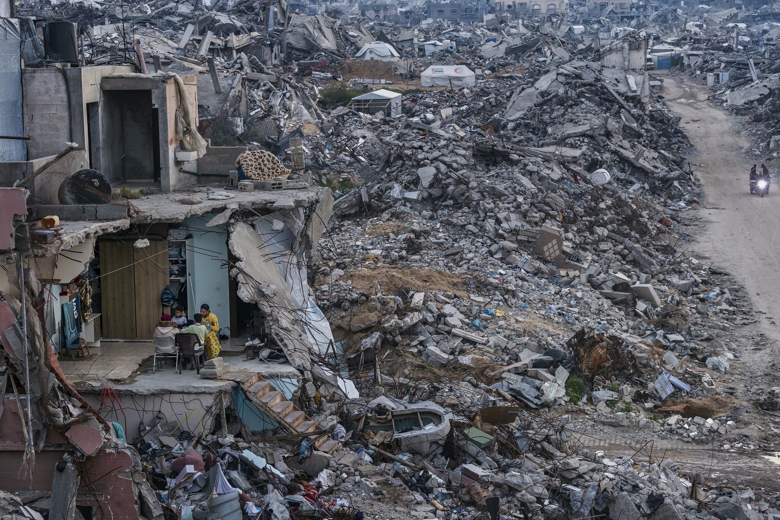 A family shares a meal in the remains of a destroyed building, situated among immense piles of rubble from other buildings in Gaza.