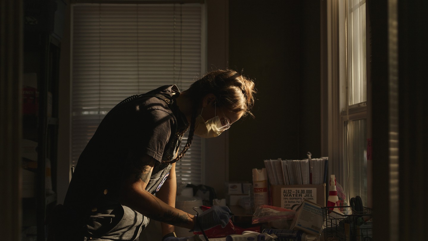 A medic leans over a desk in a darkened room, preparing medical supplies.