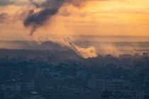 A rocket rises into a yellow, smoky sky from a darkened urban area in Gaza.