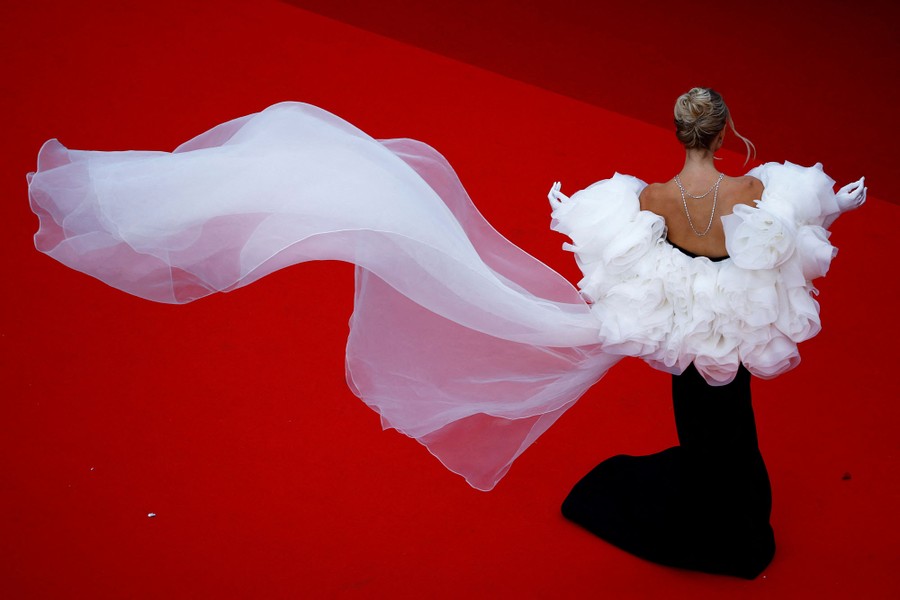 A person poses on a red carpet, the train of their dress flowing behind them.