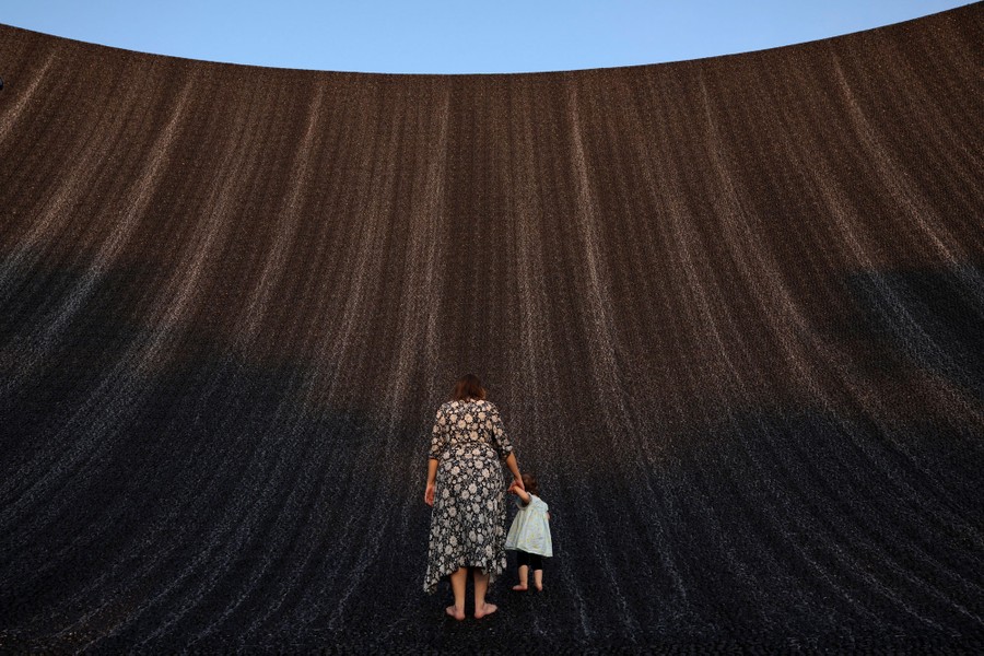 A woman and a child stand at the base of a huge curved wall, part of a fountain.