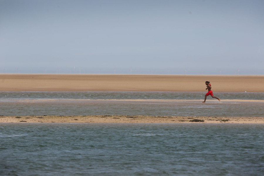 A lifeguard runs through shallow water along a broad beach.