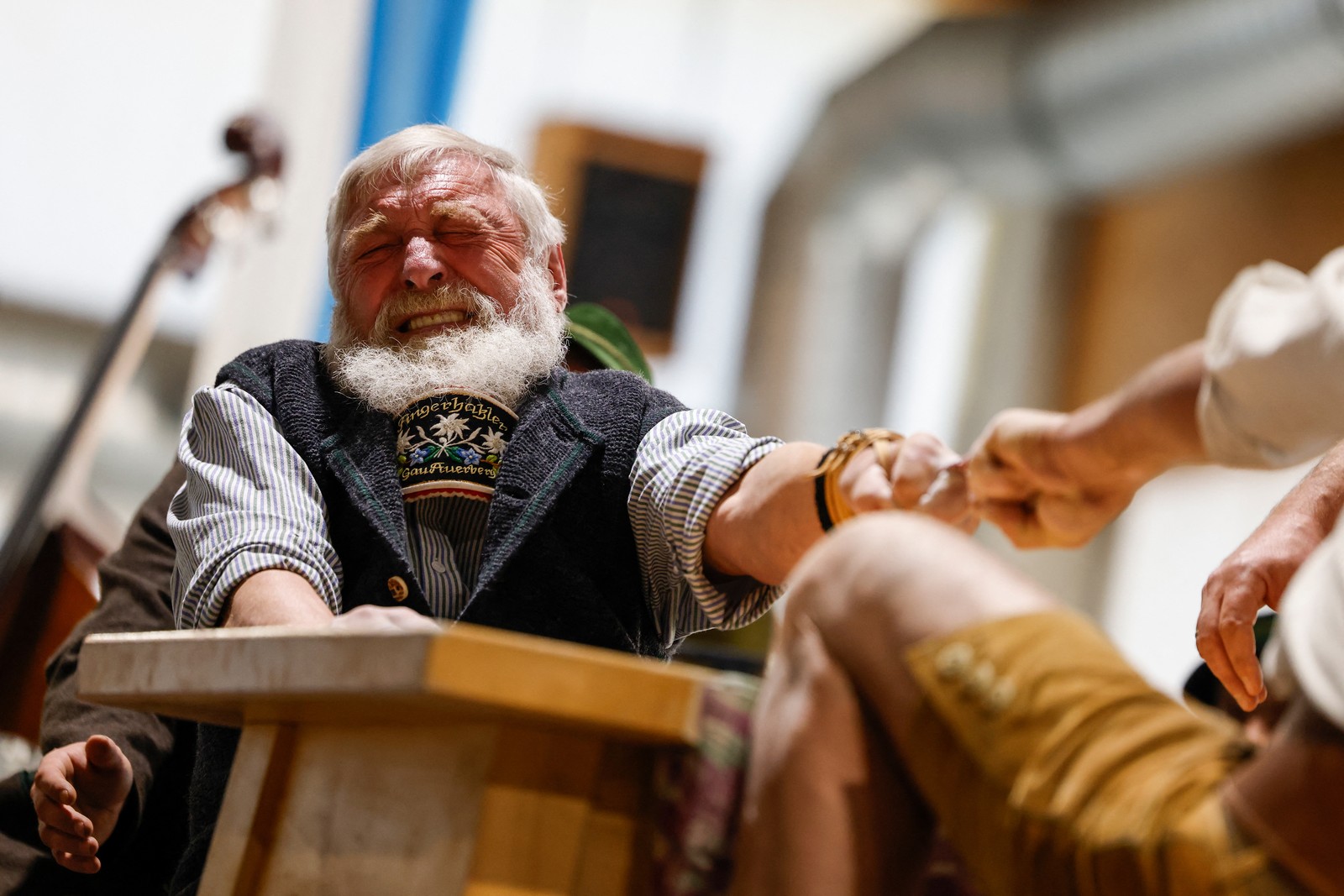 A man strains as he wrestles with another man, each pulling on a short string with one finger.