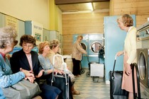 A group of older women chatting in a retro-looking laundry shop