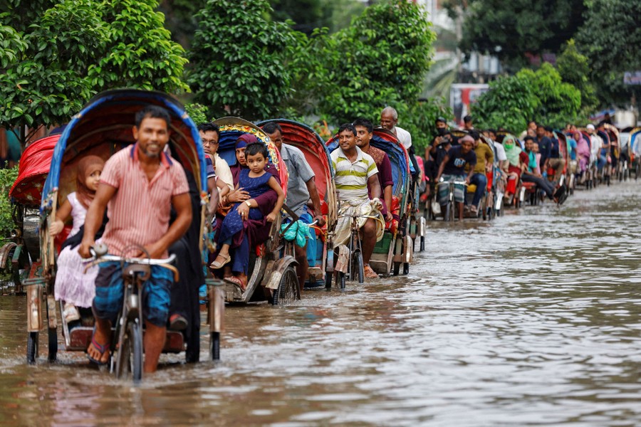 A line of commuters ride rickshaws through a flooded road.