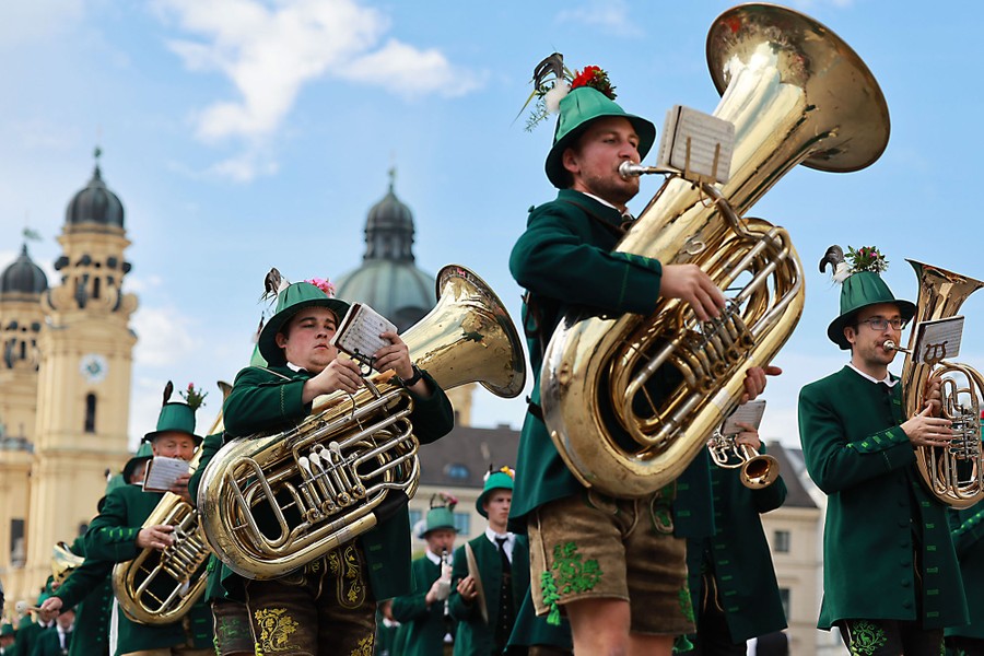 People wearing traditional Bavarian clothing march while playing brass instruments.