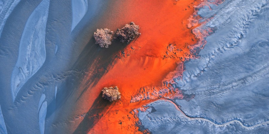 An aerial view of a barren riverbed, streaked with a section of bright reddish-orange water.