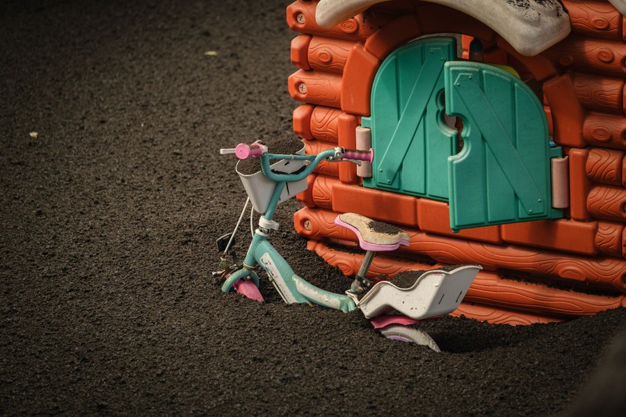 A child's bicycle sits partially buried in volcanic ash.