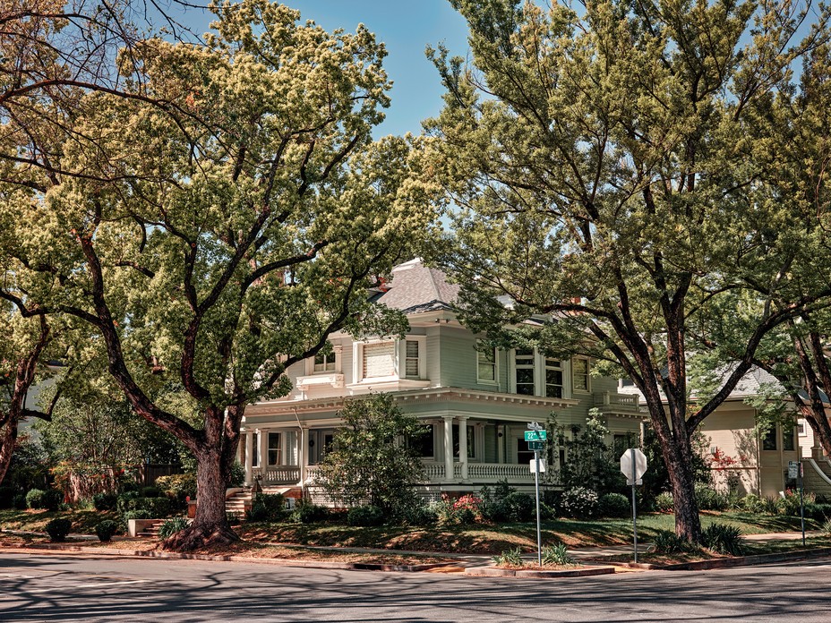 photograph of large 2-story house with porch and enormous old trees on a corner lot