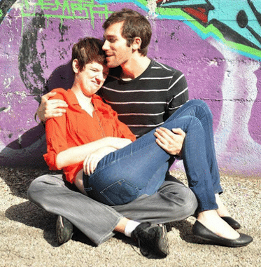 A couple sits in front of a wall with graffiti.