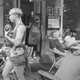 Photograph of a masked woman carrying an infant, in front of a case where no one is masked