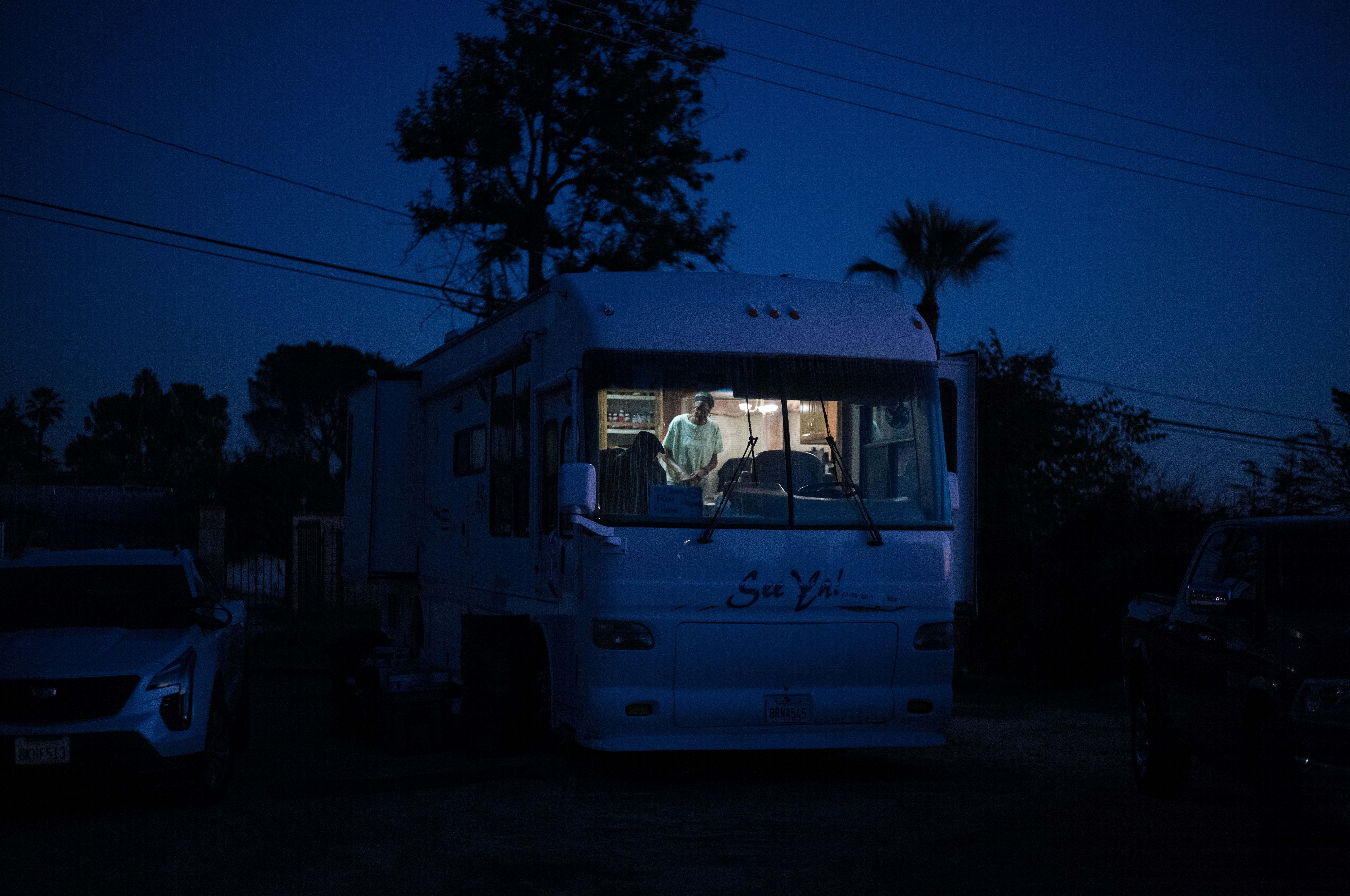 A person stands inside an RV, seen from outside at night.