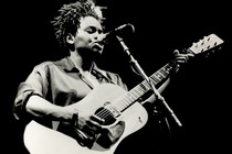 A black-and-white photo of Tracy Chapman playing the guitar and singing.