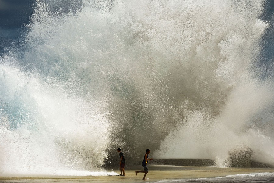 Children play in waves splashing high on a seawall.